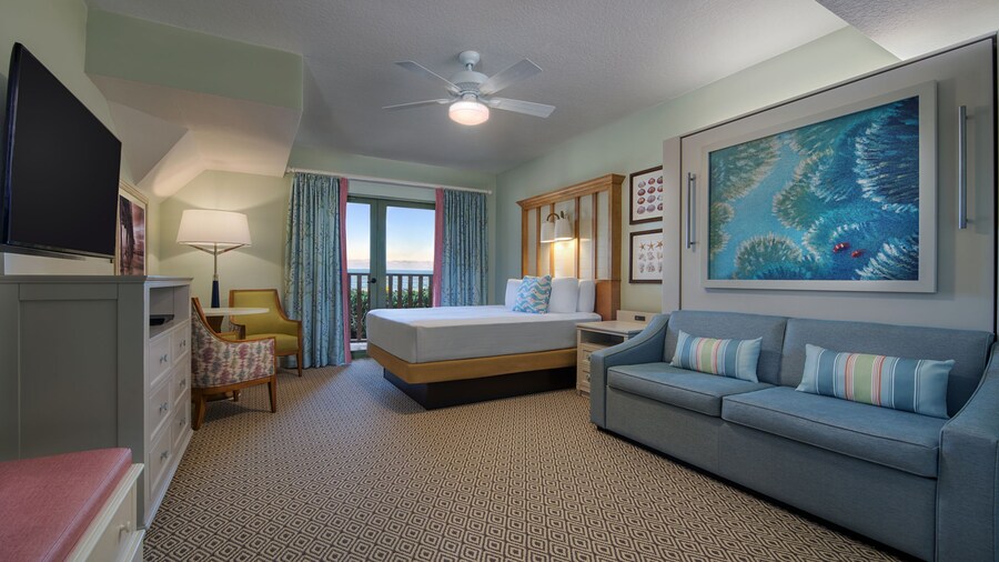 A hotel bedroom with a bed, couch, TV, a deck and aquatic artwork