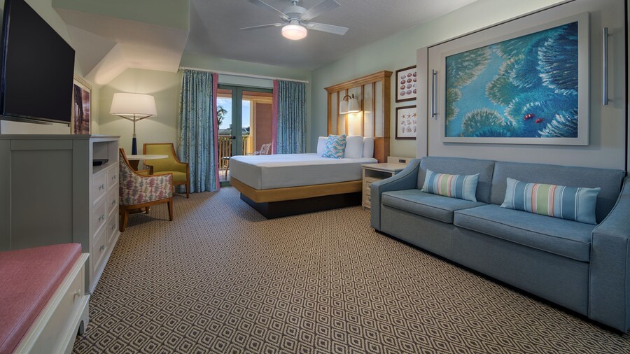 A hotel bedroom with a bed, couch, TV, a deck and aquatic artwork