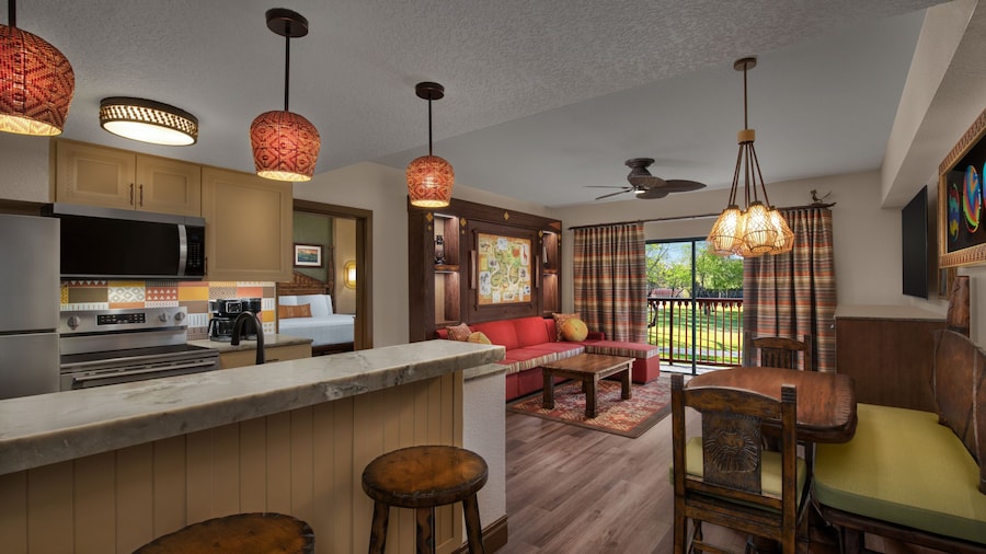 A kitchen with a stove and a living room with a view of a grassy savanna
