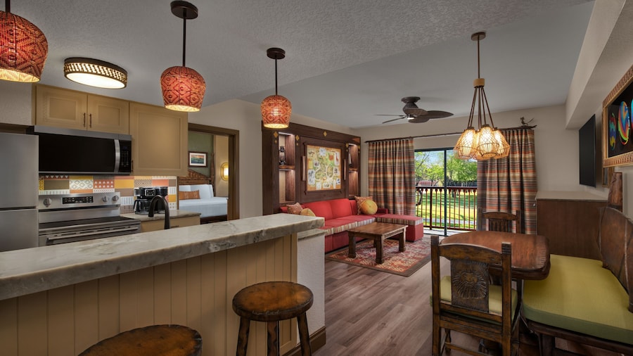 A kitchen with a stove and a living room with a view of a grassy savanna
