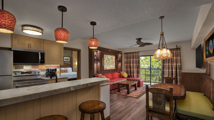 A kitchen with a stove and a living room with a view of a grassy savanna