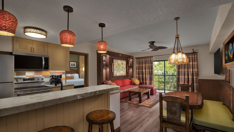 A kitchen with a stove and a living room with a view of a grassy savanna