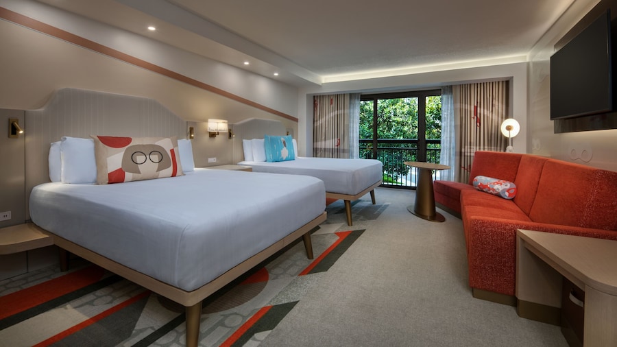 A TV cabinet, daybed, 2 queen beds and, beyond, a patio with a garden view