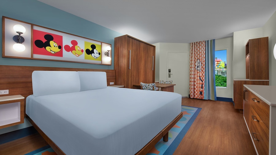 Preferred hotel room with queen sized bed next to a table and chairs overlooking the pool at Disney's Pop Century Resort