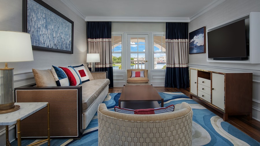 A living room with a sofa, coffee table, sideboard, TV and 2 chairs in a Commodore VP Suite at Disney’s Yacht Club Resort