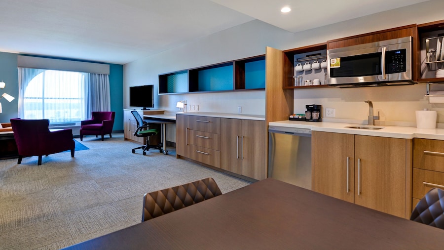 A hotel suite living room at Fairfield Inn by Marriott at Western Entrance with a full kitchen, a sofa, 2 sitting chairs, a kitchen table, A TV and a desk