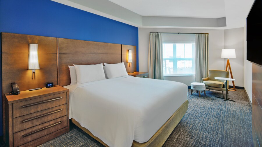 A hotel room at Fairfield Inn by Marriott at Western Entrance with a king bed, 2 wall sconces, 2 bedside tables, a TV and a chair 
