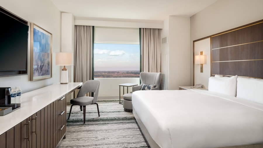 A 1 King Bed Standard Room at Signia by Hilton Orlando Bonnet Creek with a bed, a console table, a coffee maker, a TV, a chair, an armchair, a nightstand and a window with resort views
