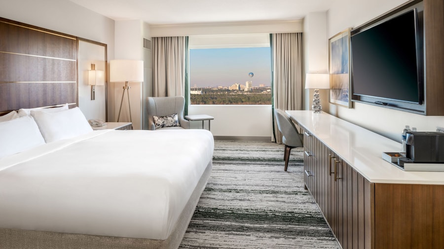 A 1 King Bed Deluxe View Standard Room at Signia by Hilton Orlando Bonnet Creek with a bed, a nightstand, an armchair, a console table, a TV, a coffee maker and a window with resort views