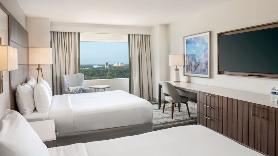 A 2 Queen Bed Deluxe View Standard Room at Signia by Hilton Orlando Bonnet Creek with 2 beds, a nightstand, an armchair, a console table, a TV and a window with resort views