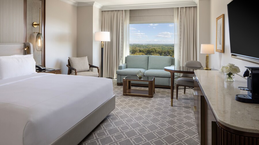 A 1 King Bed Deluxe Room at Waldorf Astoria Orlando with a bed, a nightstand, an armchair, a sofa, a low table, a desk, a console table, a TV and a window with resort views