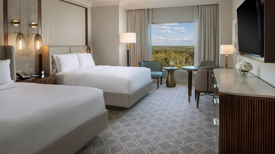 A 2 Queen Beds Deluxe Room at Waldorf Astoria Orlando with 2 beds, a nightstand, a chair, a desk, a console table, a TV and a window with resort views