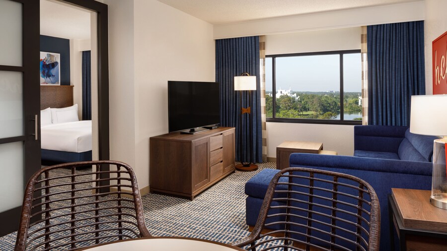 A living room with a dining table, a lamp, a sofa, a TV, a cabinet, a window with exterior views and a sliding door in a room at the DoubleTree Suites by Hilton Orlando