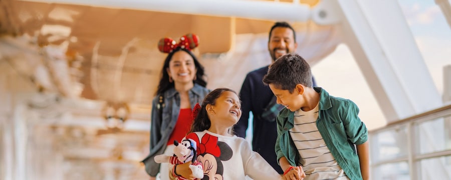 Smiling family in Disney themed attire walking together on the deck of a Disney Cruise Line ship
