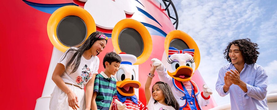 Una joven familia de cuatro personas bailando con Donald y Daisy en la cubierta de un crucero de Disney Cruise Line  