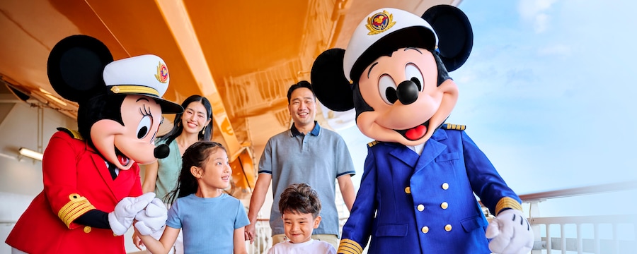 A couple overlooking Captain Mickey and Captain Minnie holding hands with their 2 children as they walk on the deck of a Disney cruise ship