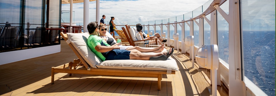 A group of people sunbathing on loungers on the deck of the Disney Wish cruise ship