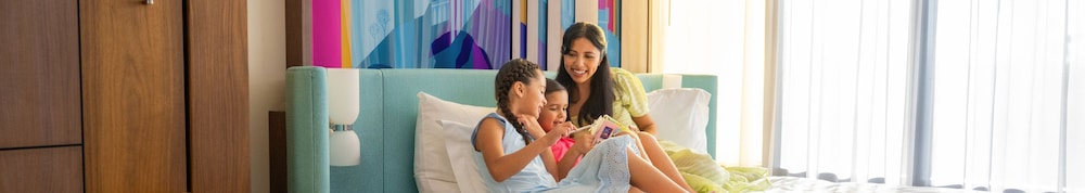 A mother and her 2 children lounge on a hotel bed at the Disneyland Resort