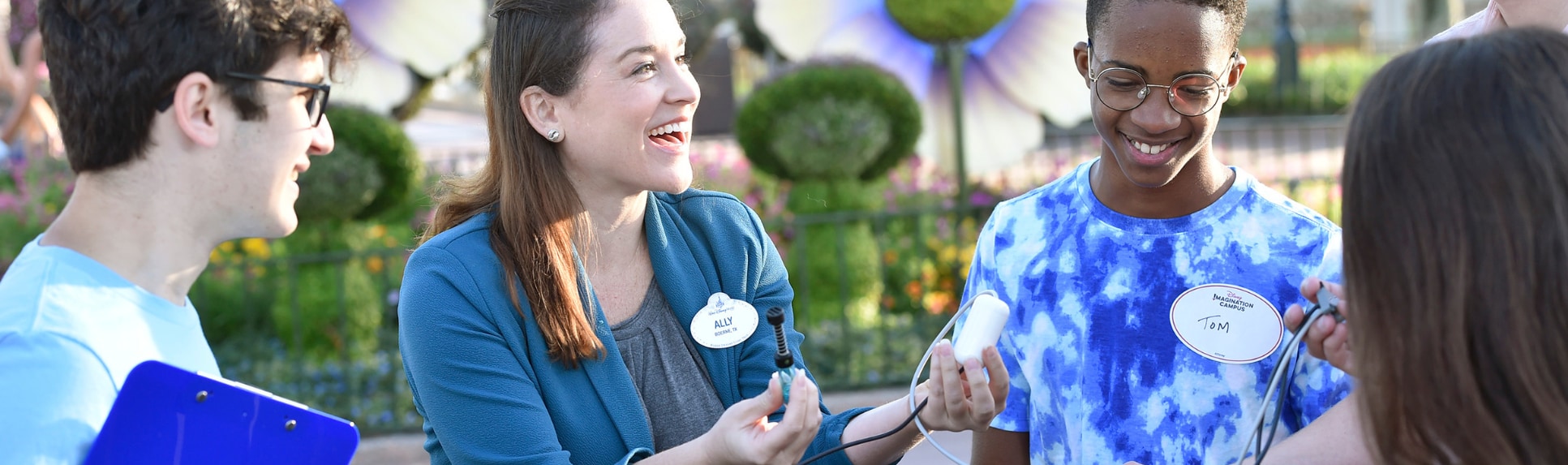 A Cast Member holding wires and equipment talks to 2 Disney Imagination Campus students