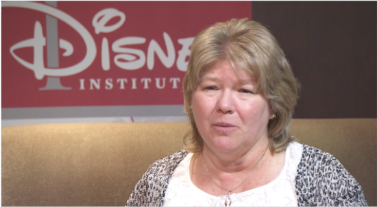 A talking woman seated on a couch in front of the Disney Institute sign