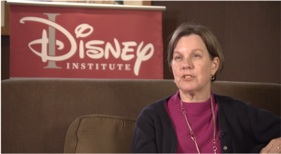 A talking woman seated on a couch in front of the Disney Institute sign
