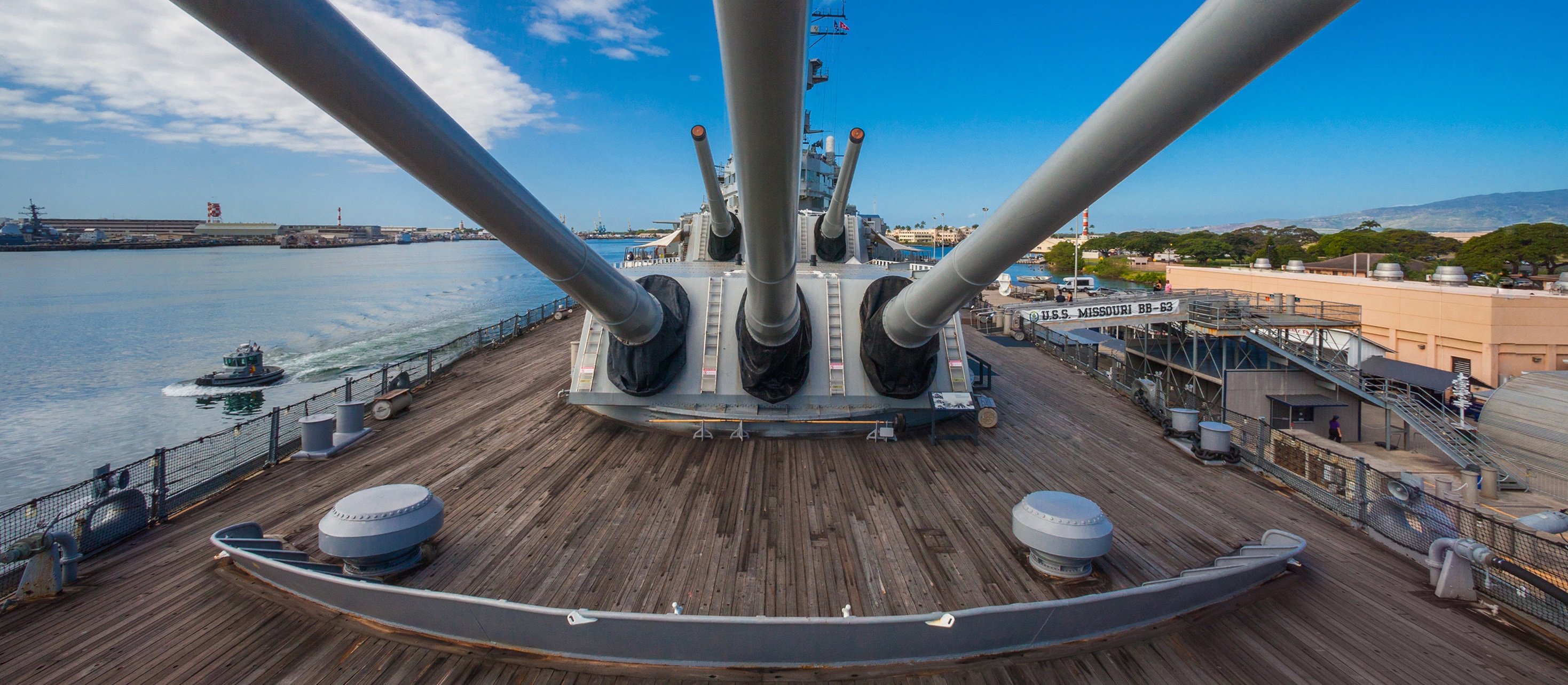 Aboard the deck of the battleship U S S Missouri, the barrels of 5 high-caliber guns are aimed skyward
