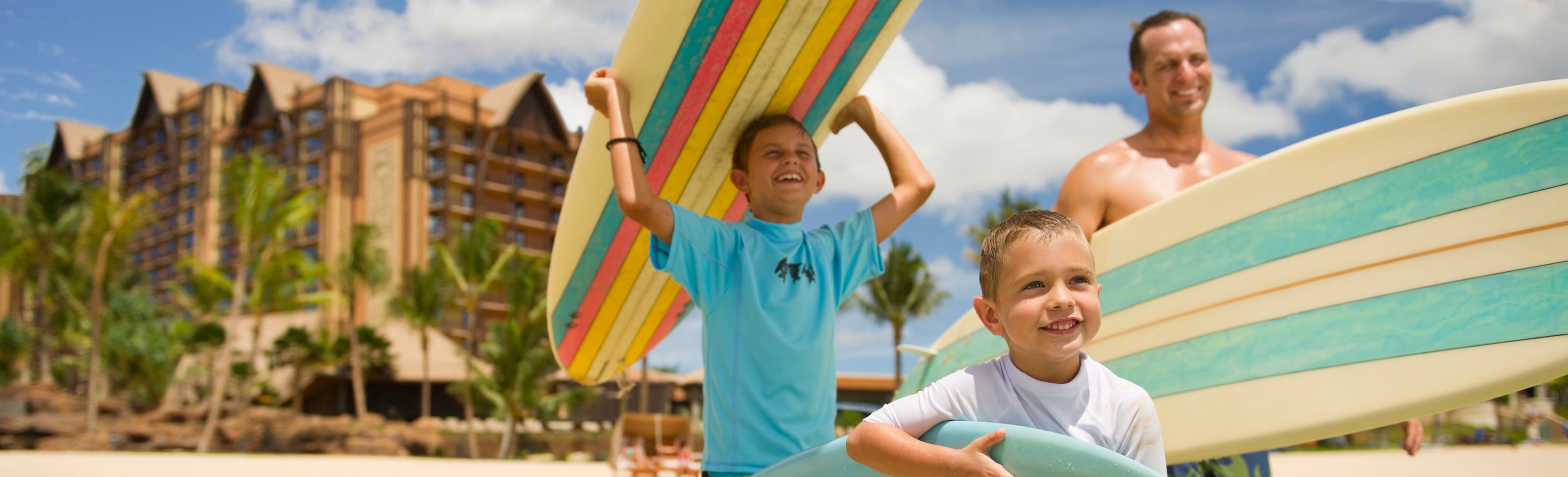 A father and his 2 young sons head toward the ocean carrying surfboards
