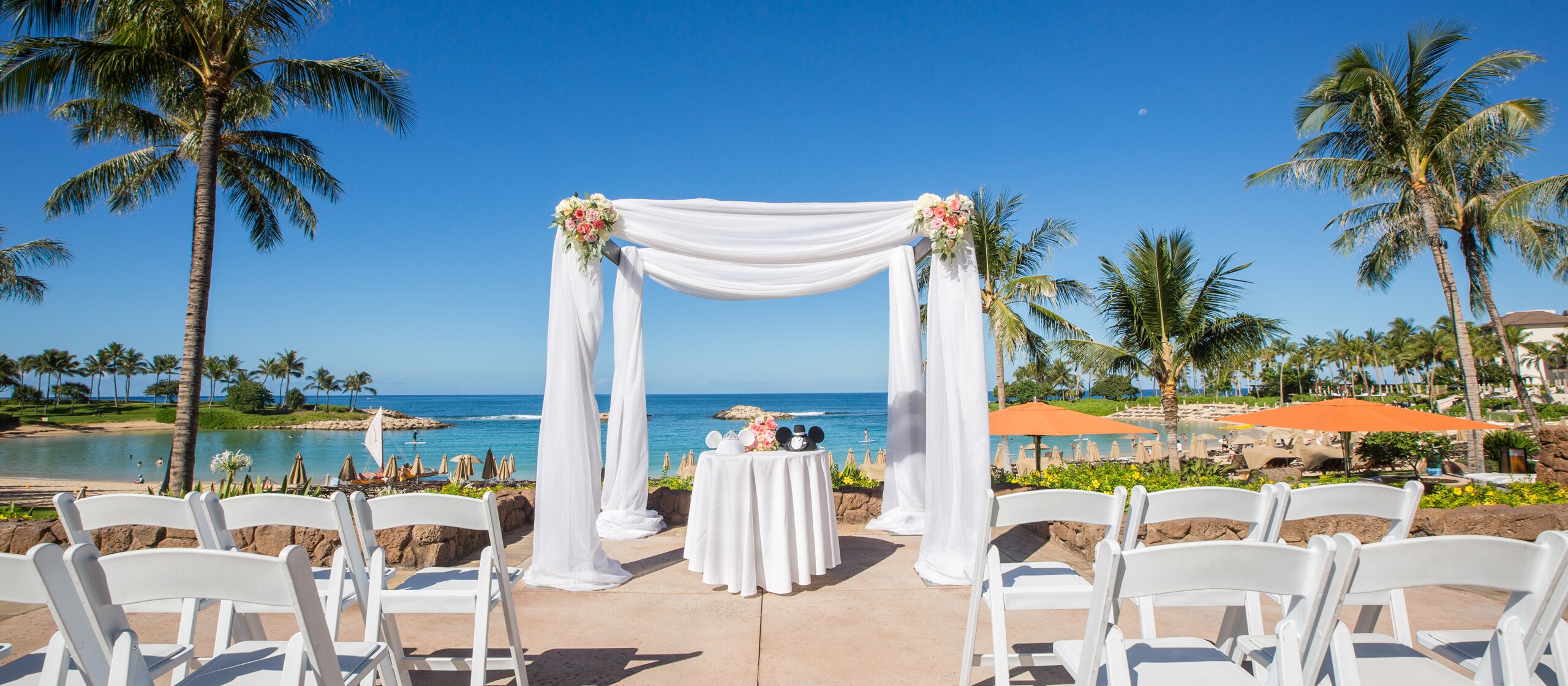 An Aulani Resort outdoor courtyard area overlooking the ocean is dressed for a wedding with an altar and folding chairs