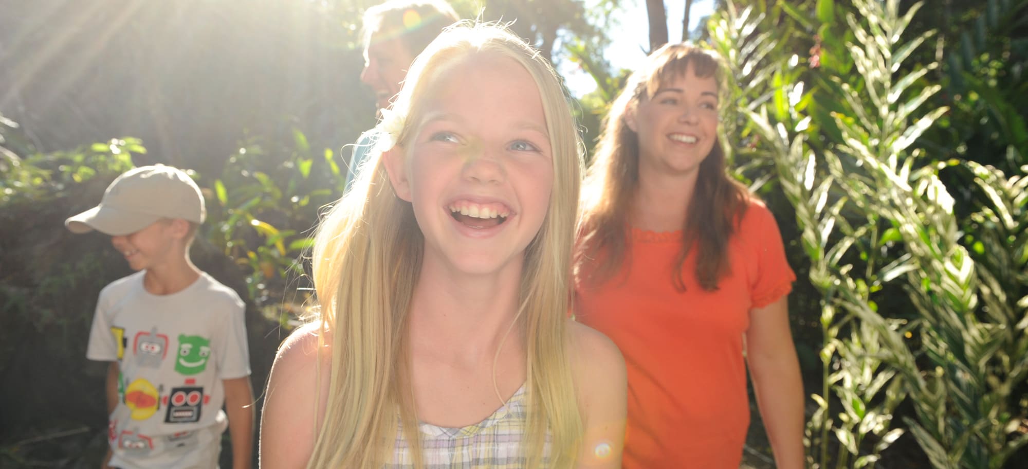 A smiling girl leads her mother, father and brother on a sun-dappled path through a tropical forest