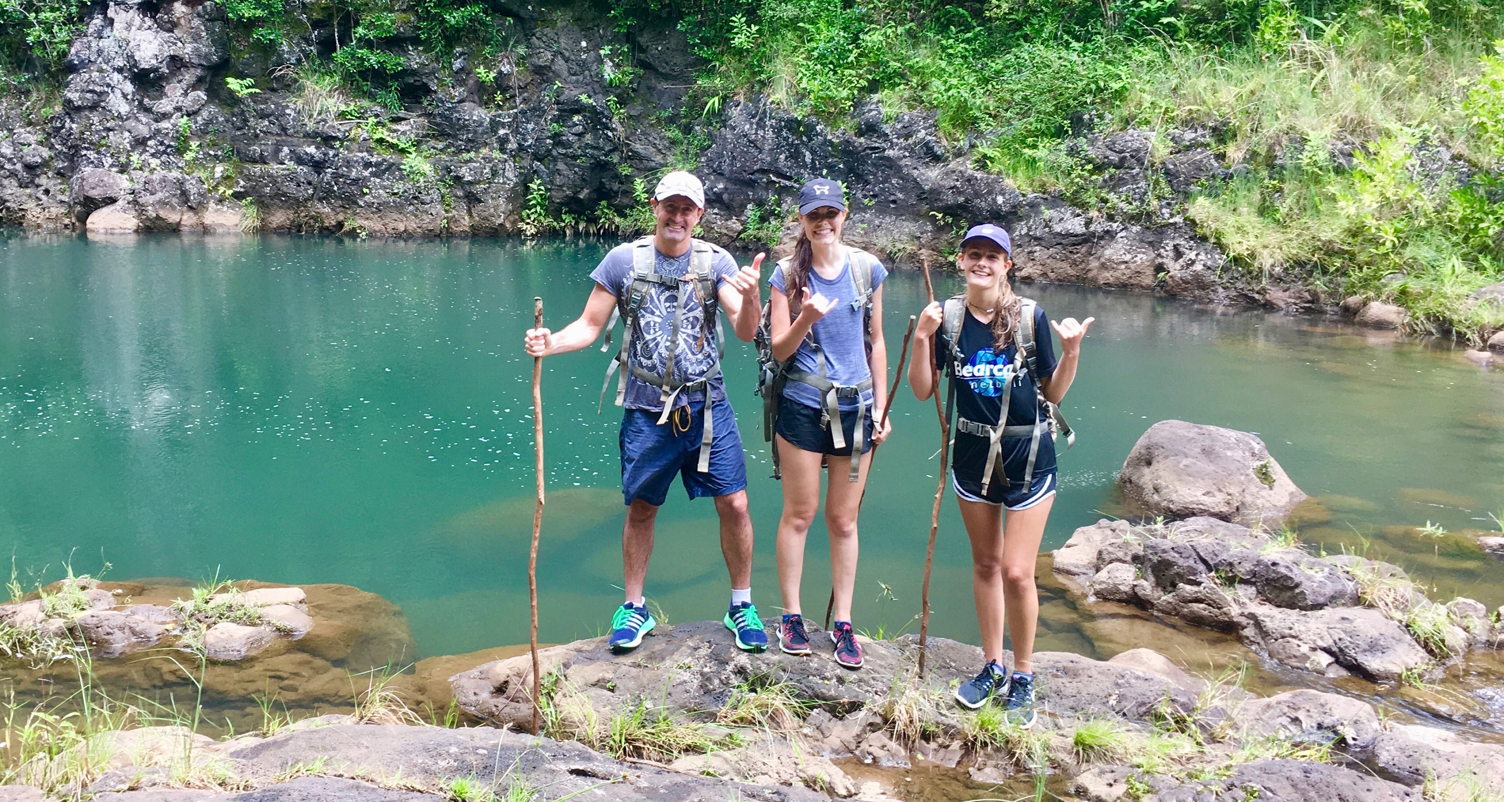 Three hikers stand near a creek surrounded by foliage and rocks