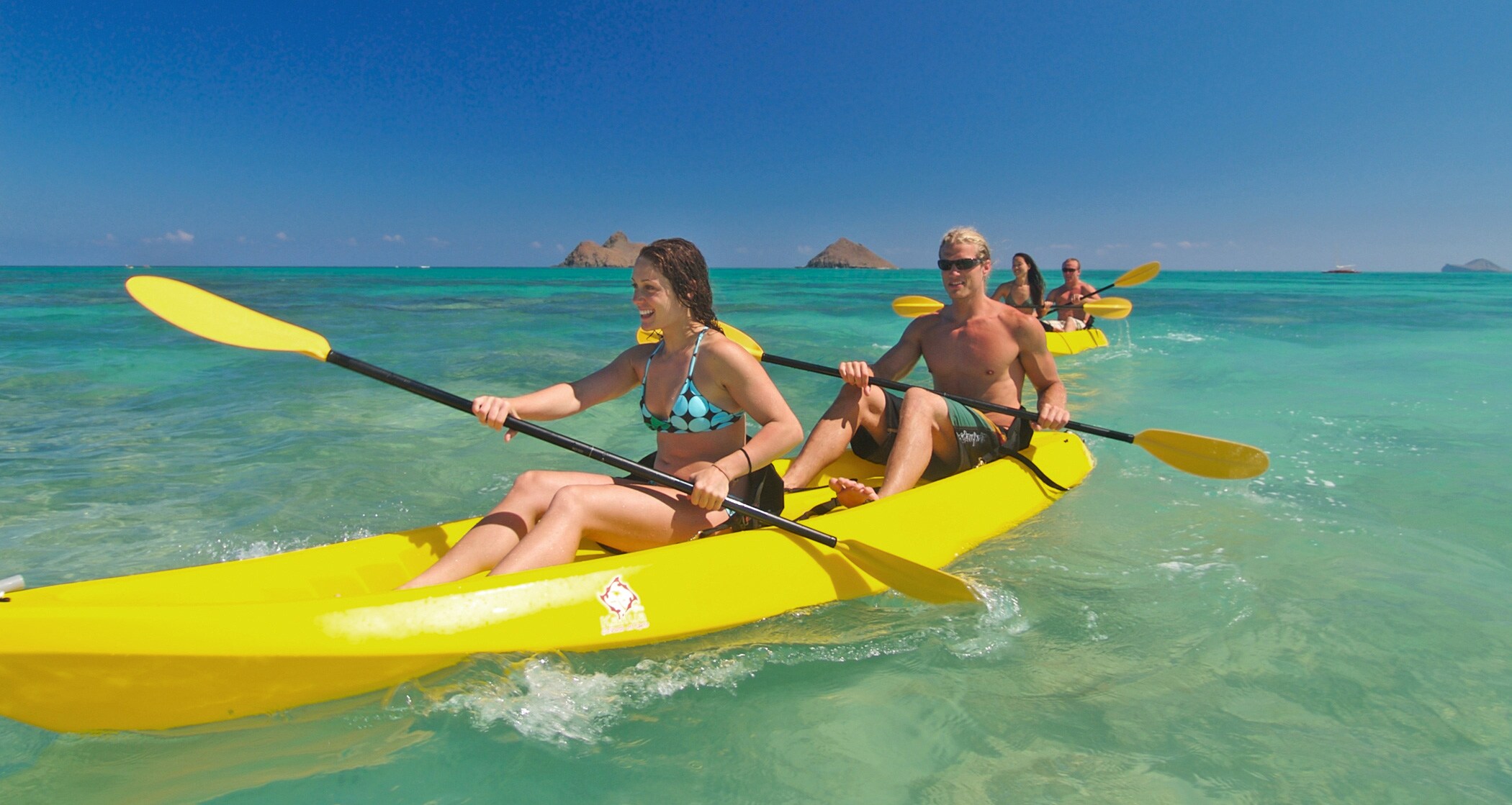 Two couples paddle their kayaks in the open ocean