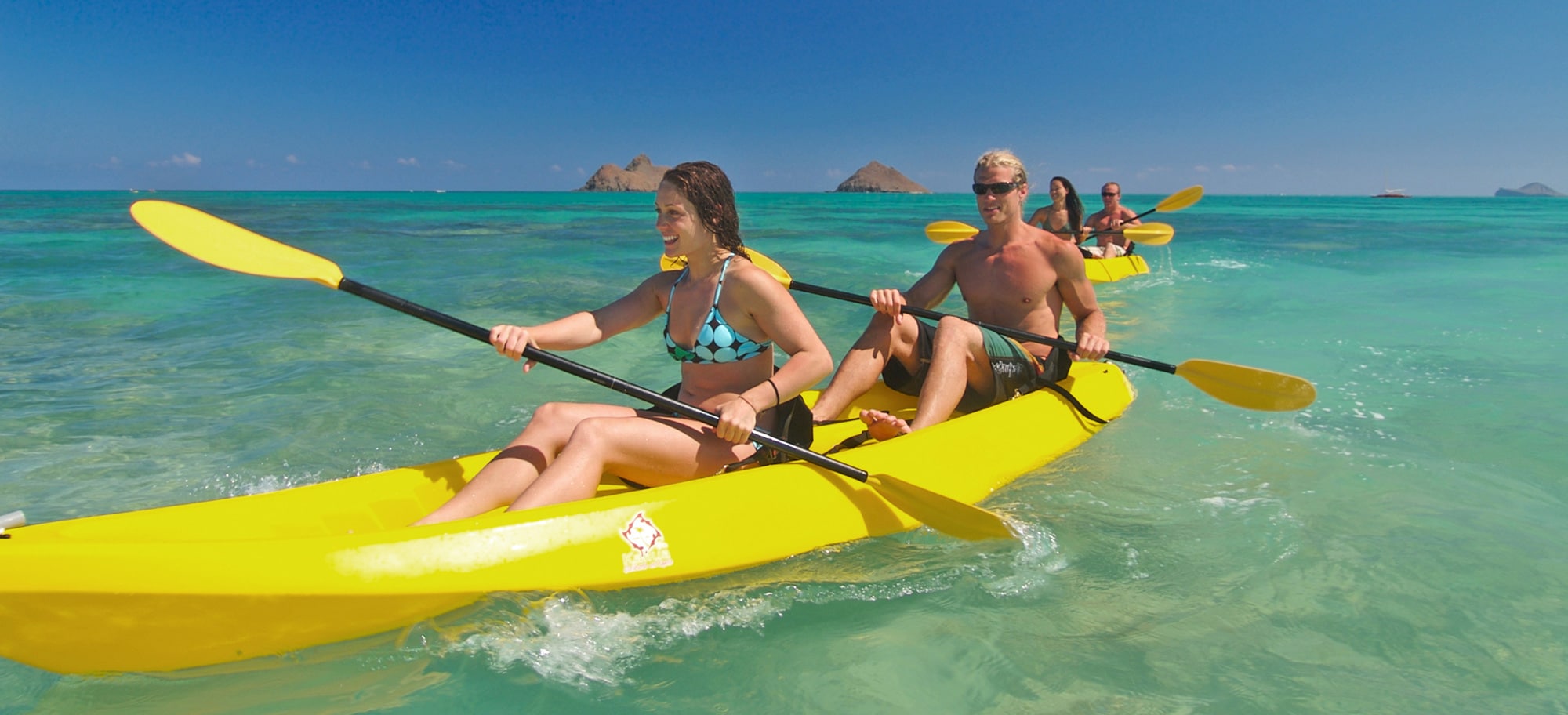 Two couples paddle their kayaks in the open ocean
