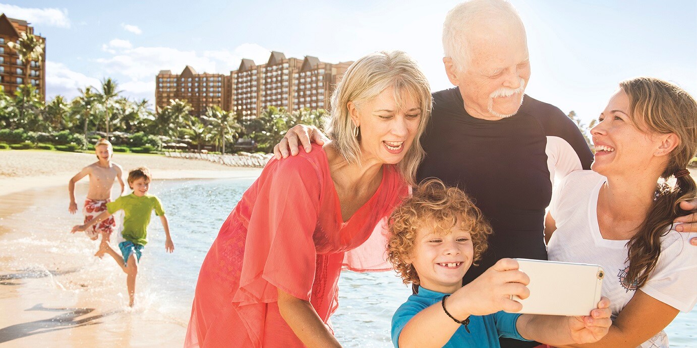 A small kid and his family in the beach watching a cell phone