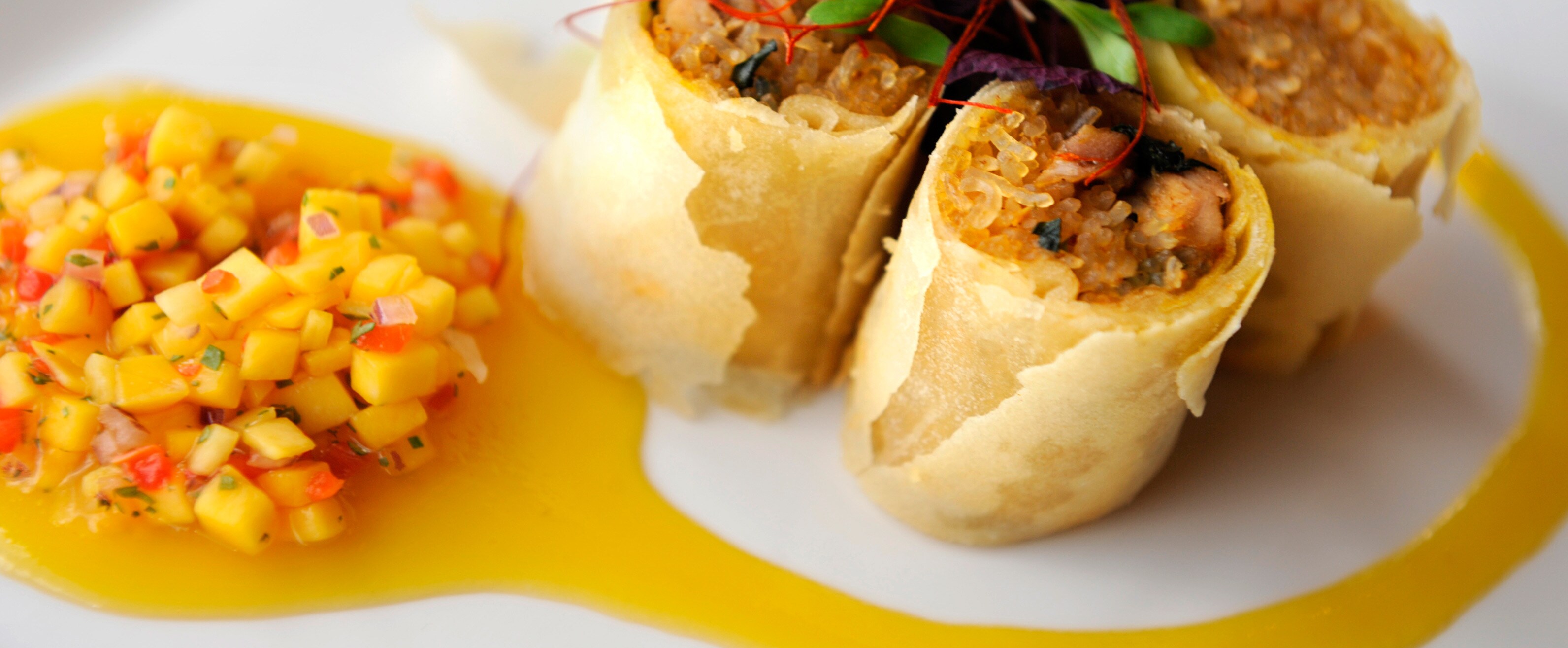 An egg roll cut into 3 pieces on a white plate garnished with mango salsa