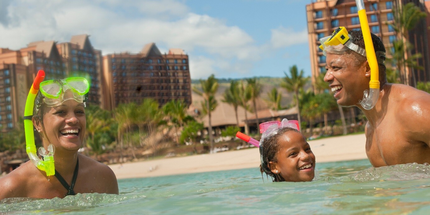 A man, woman and their daughter snorkeling in the lagoon at Aulani Resort