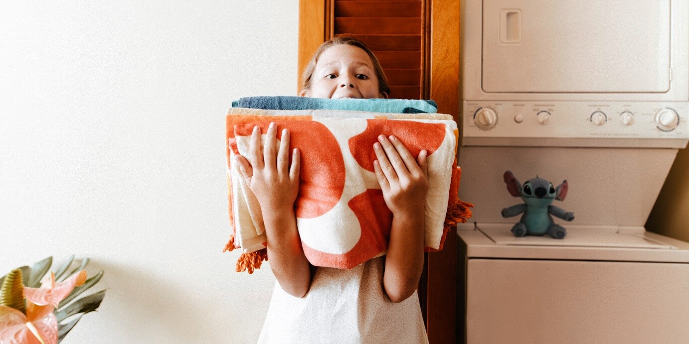 A young girl holding a stack of towels in the laundry area of a Villa