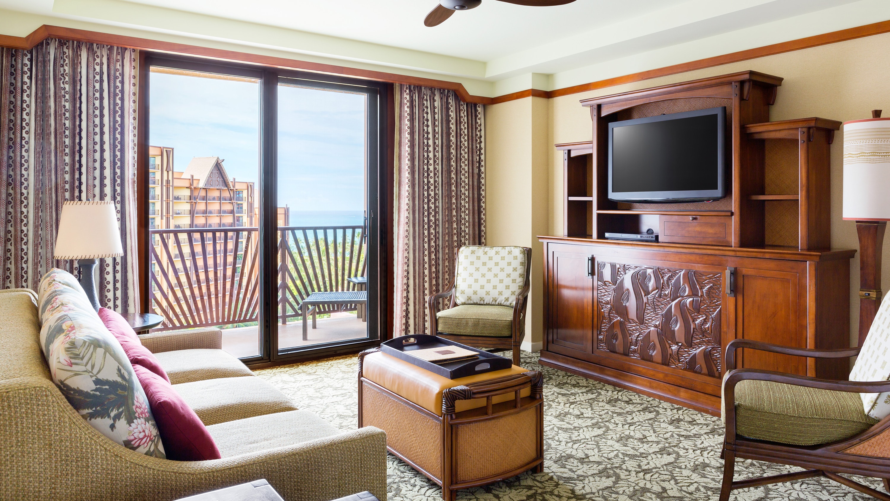 A room with a couch, an ottoman, 2 lamps, 2 chairs, a TV and balcony access