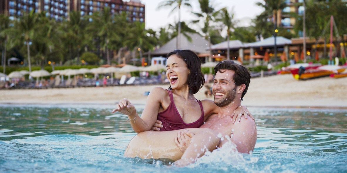 A man carrying a woman into the lagoon at Aulani Resort