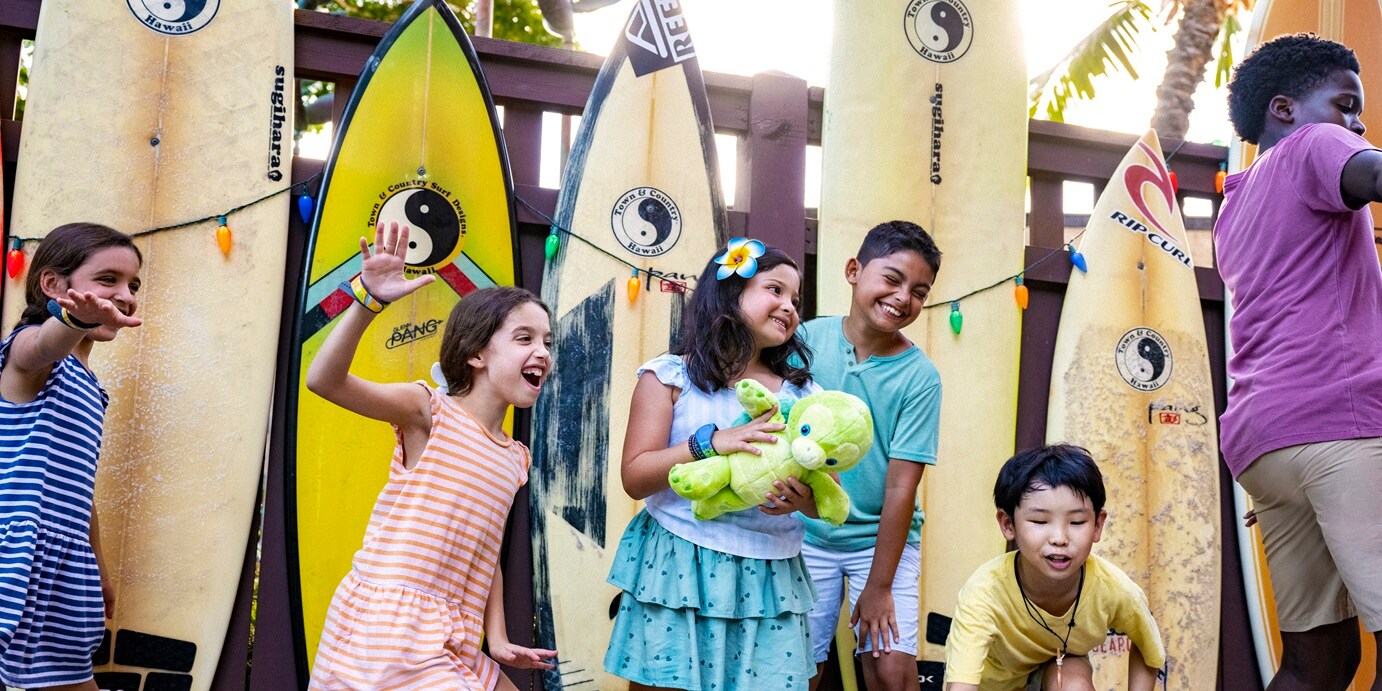 Several children smiling and playing with surf boards in their back