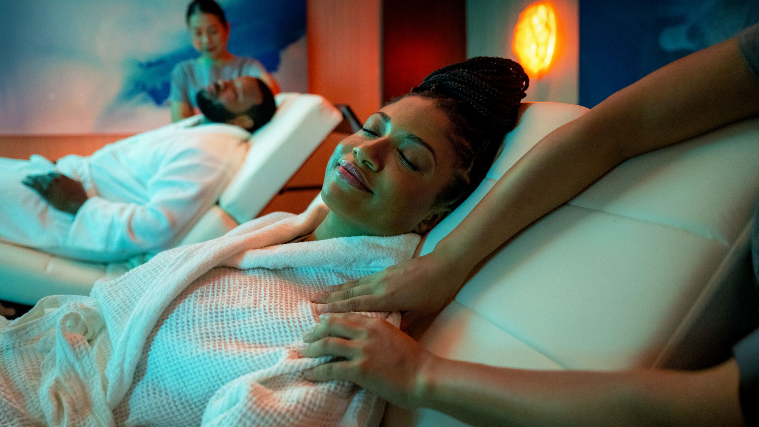 Two people lying on chairs with their eyes closed while getting a shoulder massage
