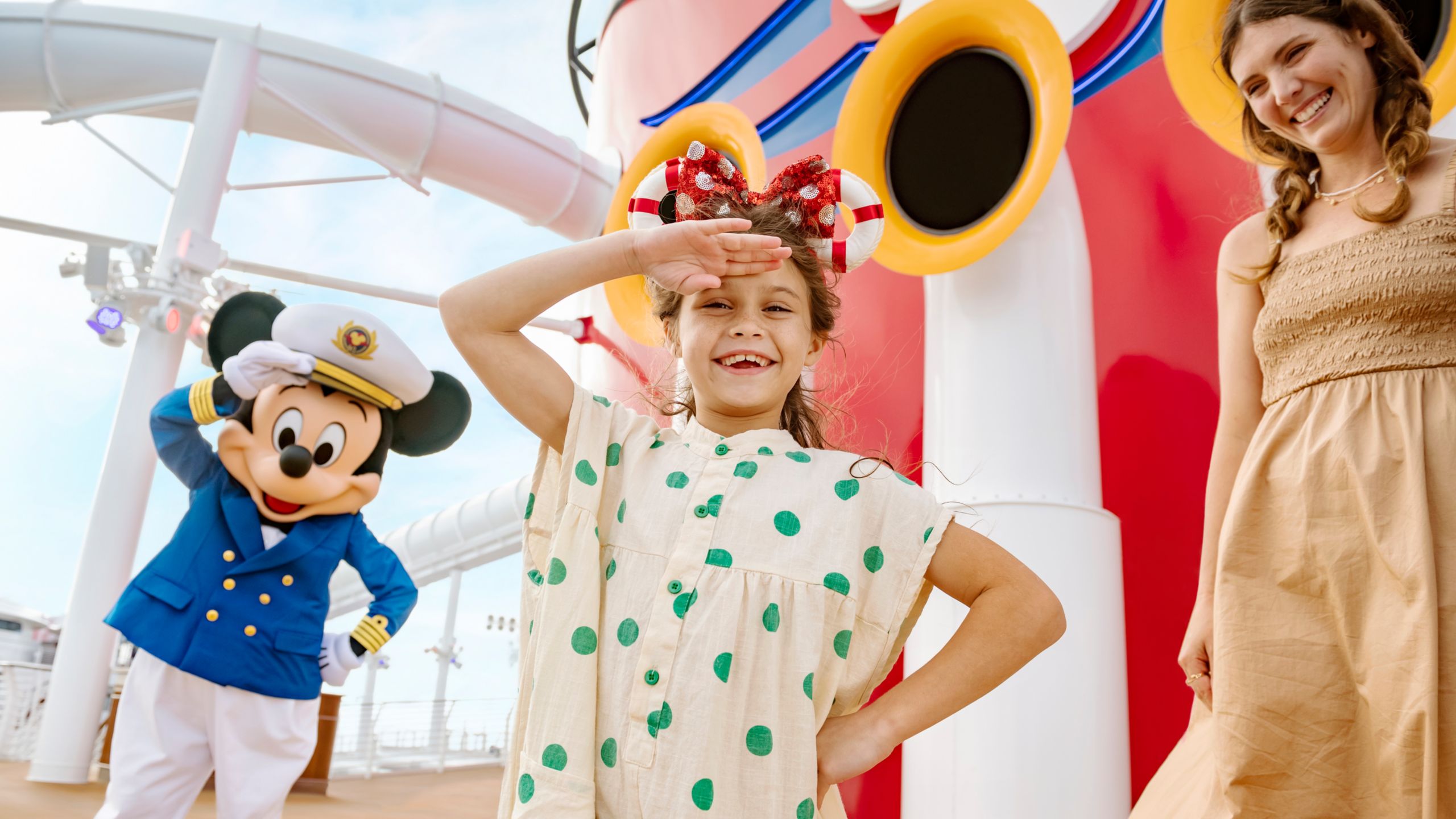 A girl doing a salute pose while wearing a Minnie Mouse Ear Headband with Mickey Mouse in the background