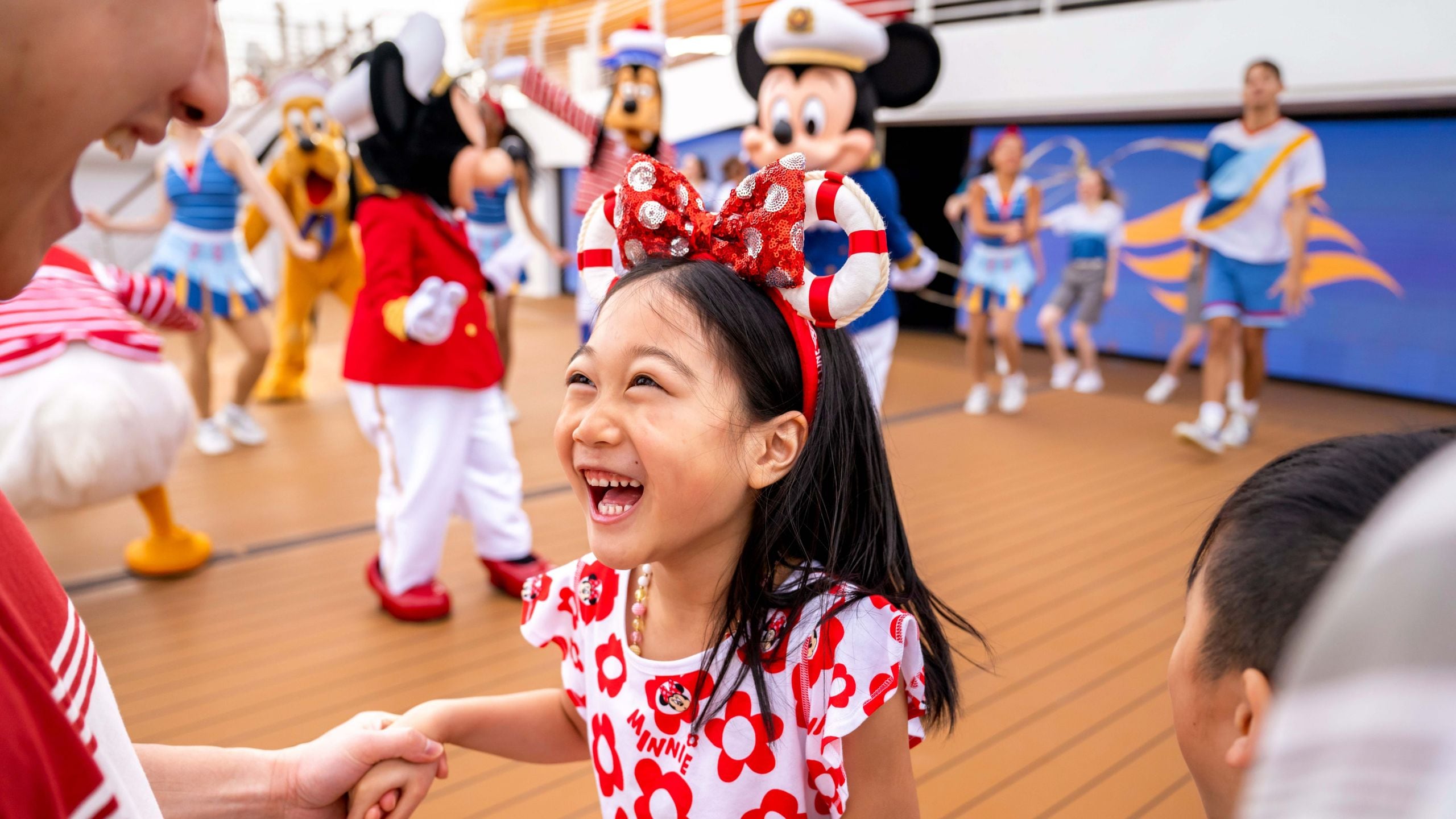 A young girl dancing and holding hands with their parent in front of dancing Disney Characters