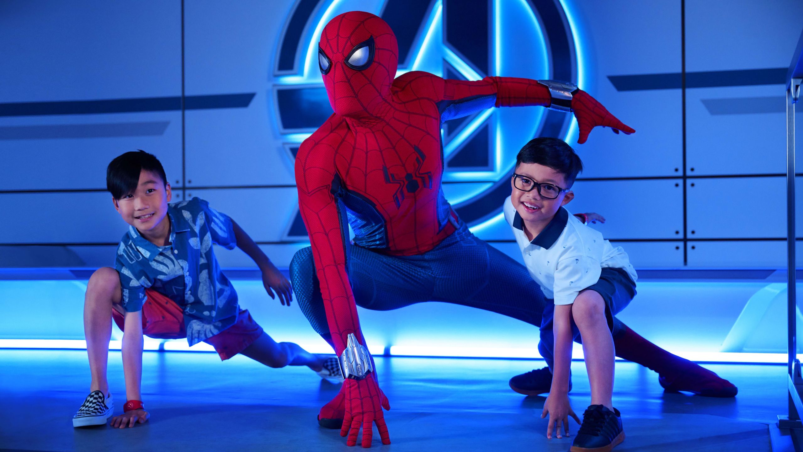 Two young boys and Spider Man posing together in front of an illuminated Avengers logo