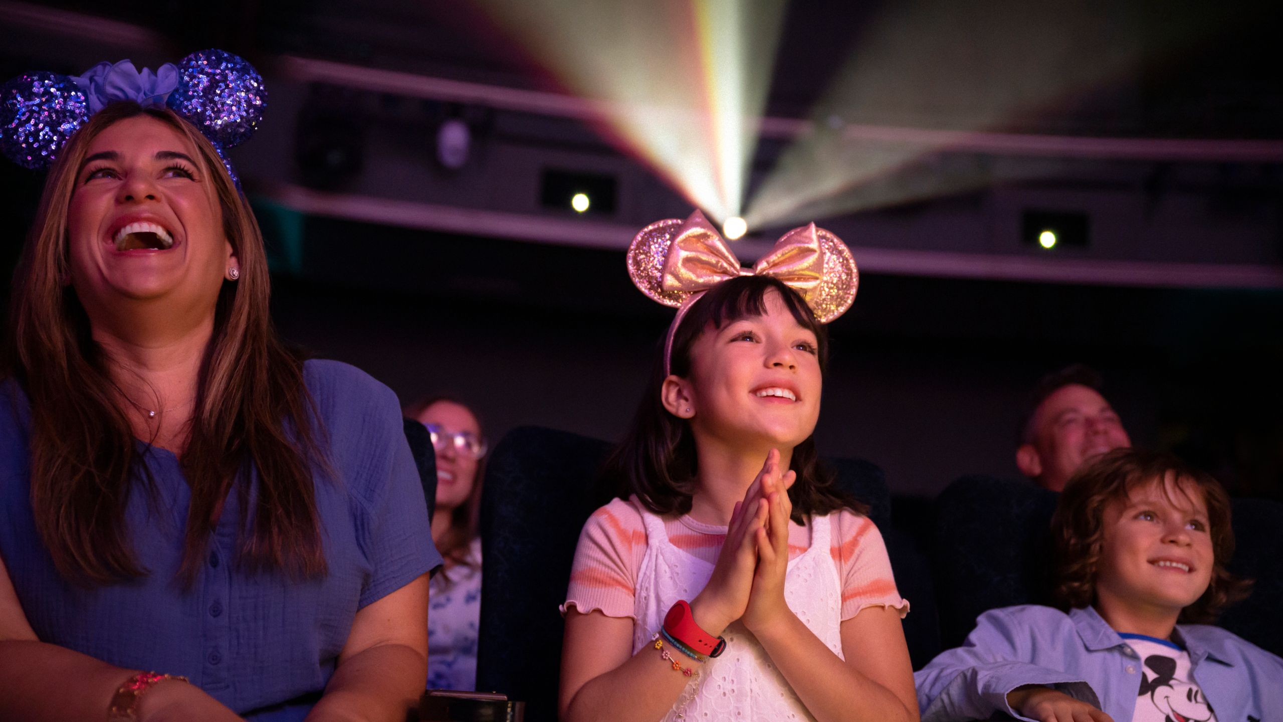 A woman and 2 children smiling while watching a film in a theater