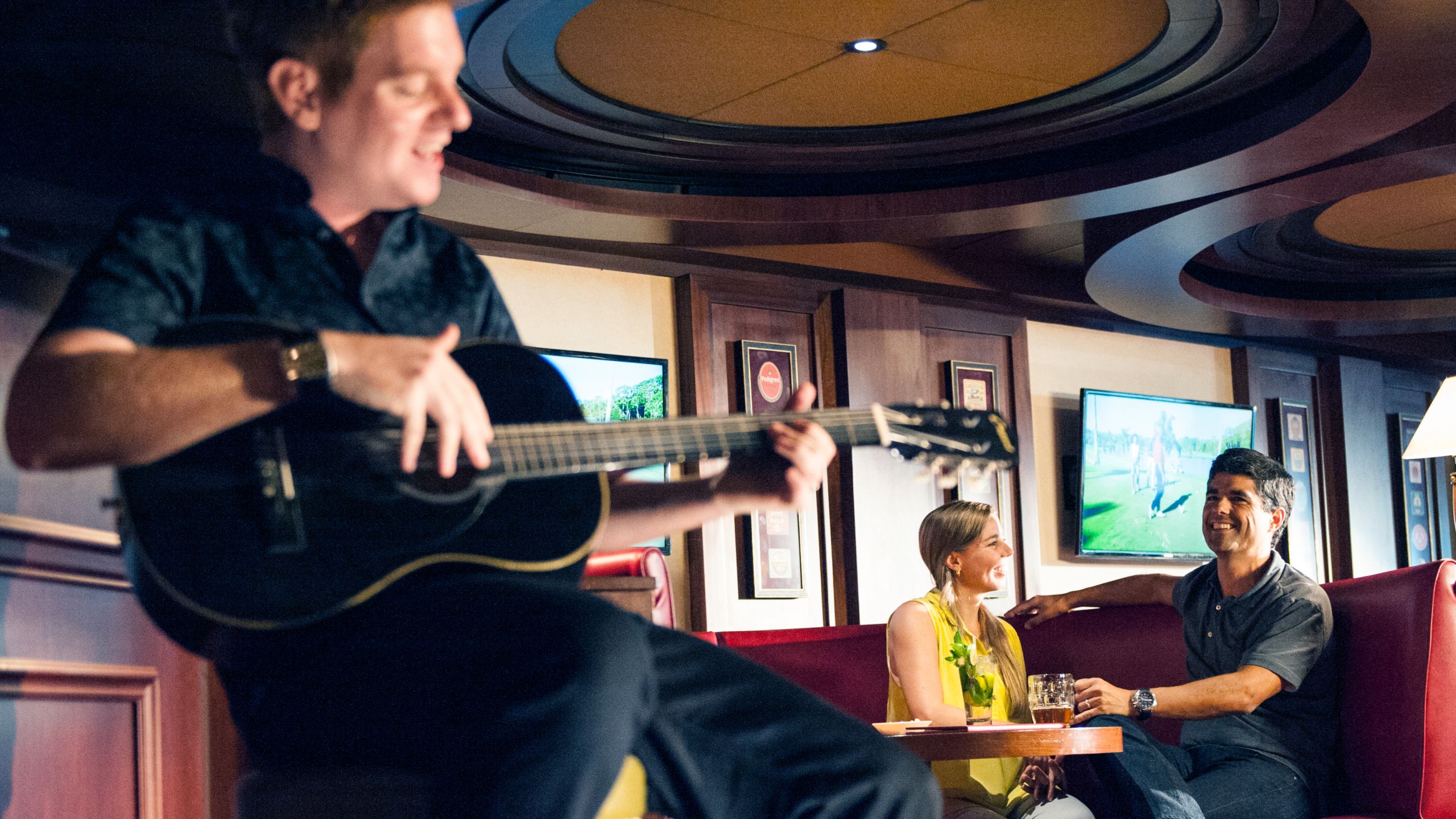 A musician playing guitar while a man and woman sit and watch from a nearby table