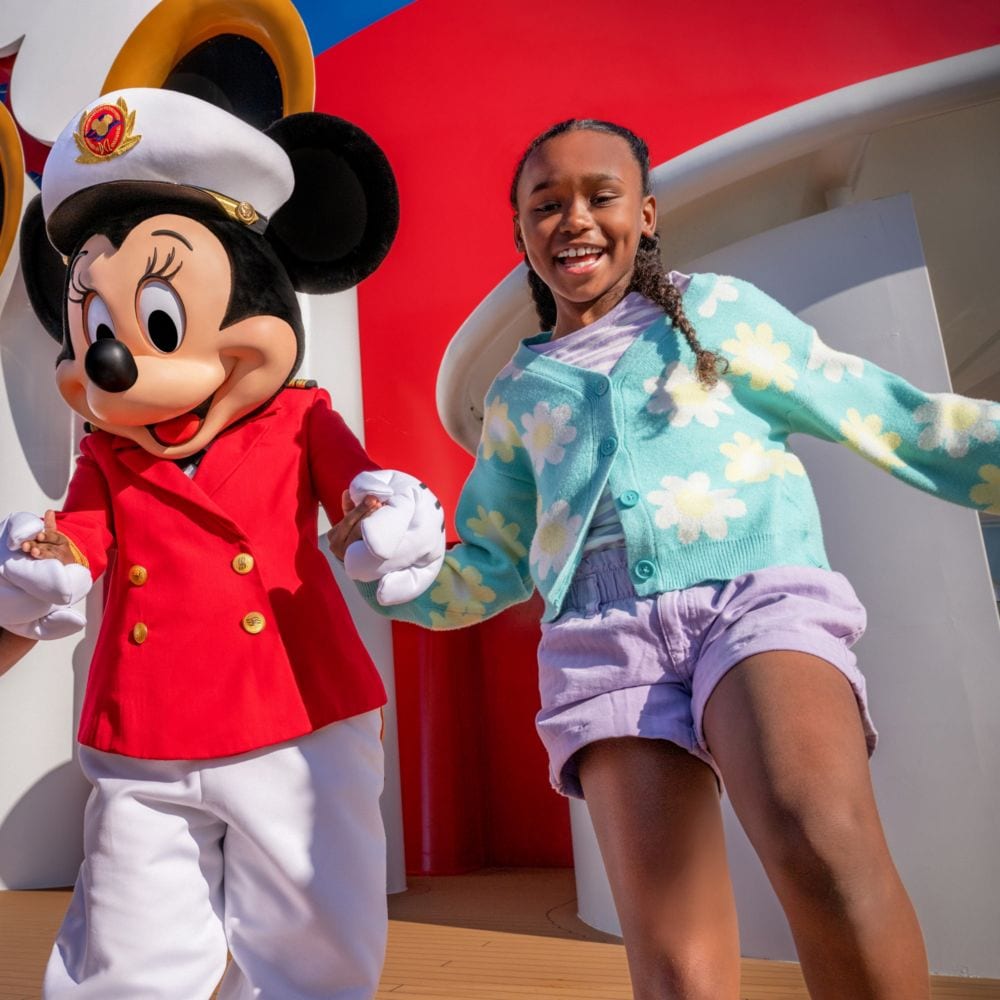 A girl holding hands with Captain Minnie Mouse while standing on the deck of a Disney Cruise Line ship
