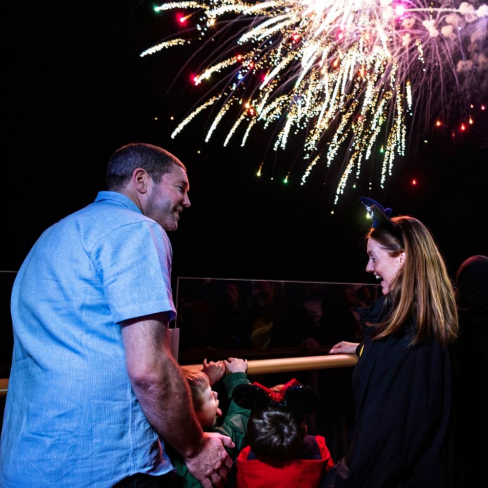 A family watches a vibrant fireworks display in a dark sky