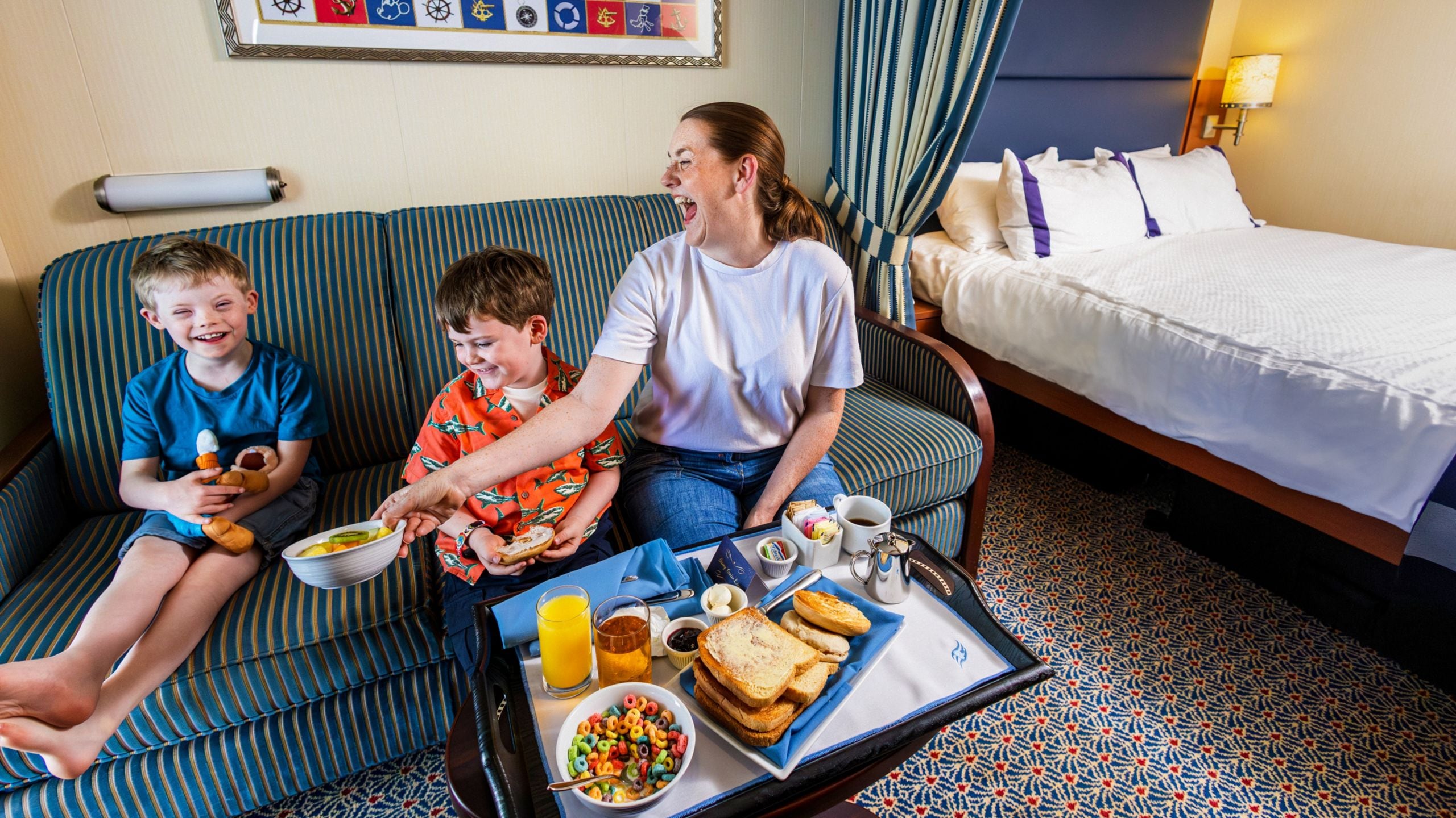 A mother and her 2 young boys enjoying a meal while sitting on a sofa in a hotel room