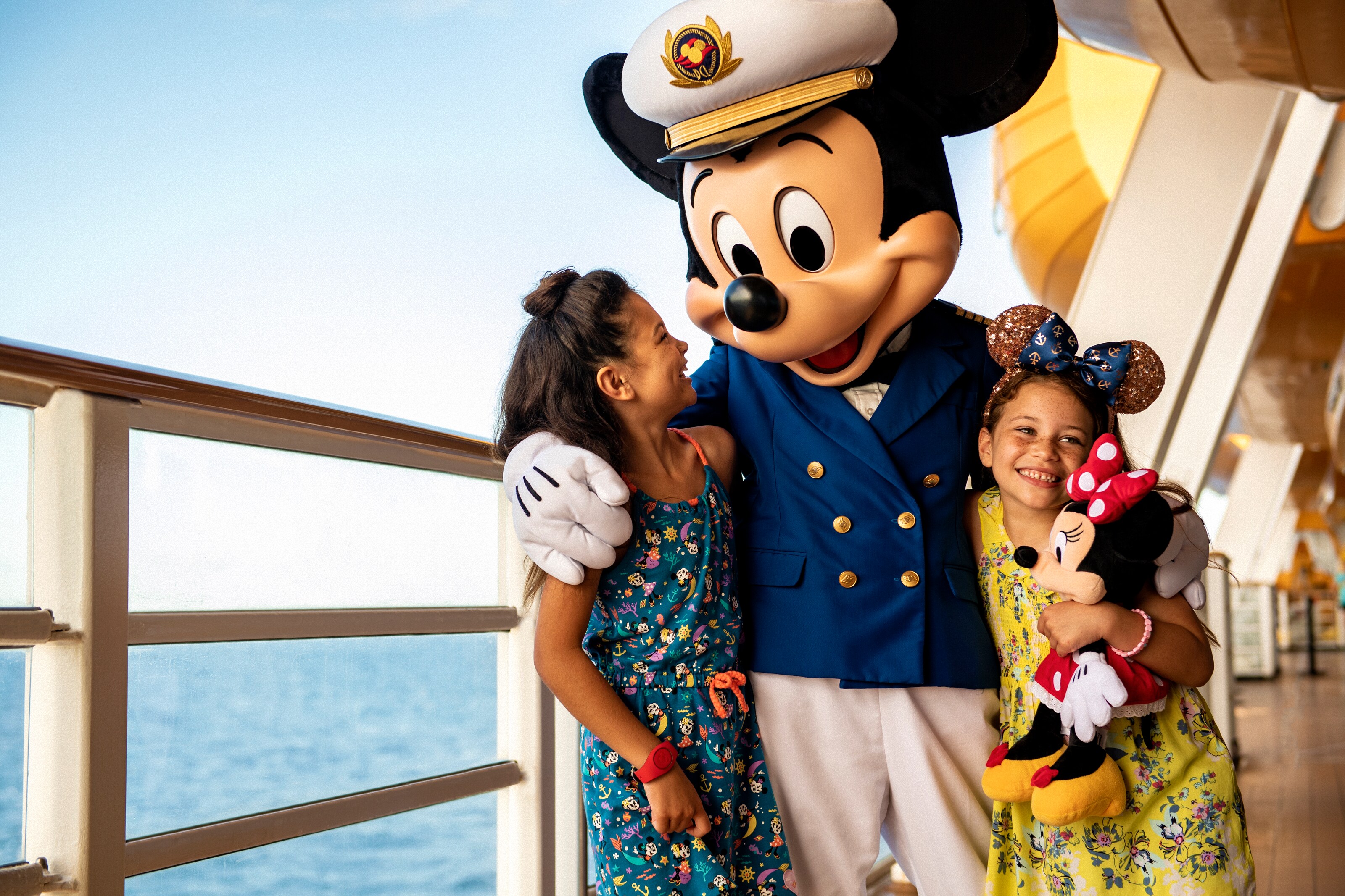 El Capitán Mickey con los brazos alrededor de dos niñas en la cubierta de un barco de Disney Cruise Line