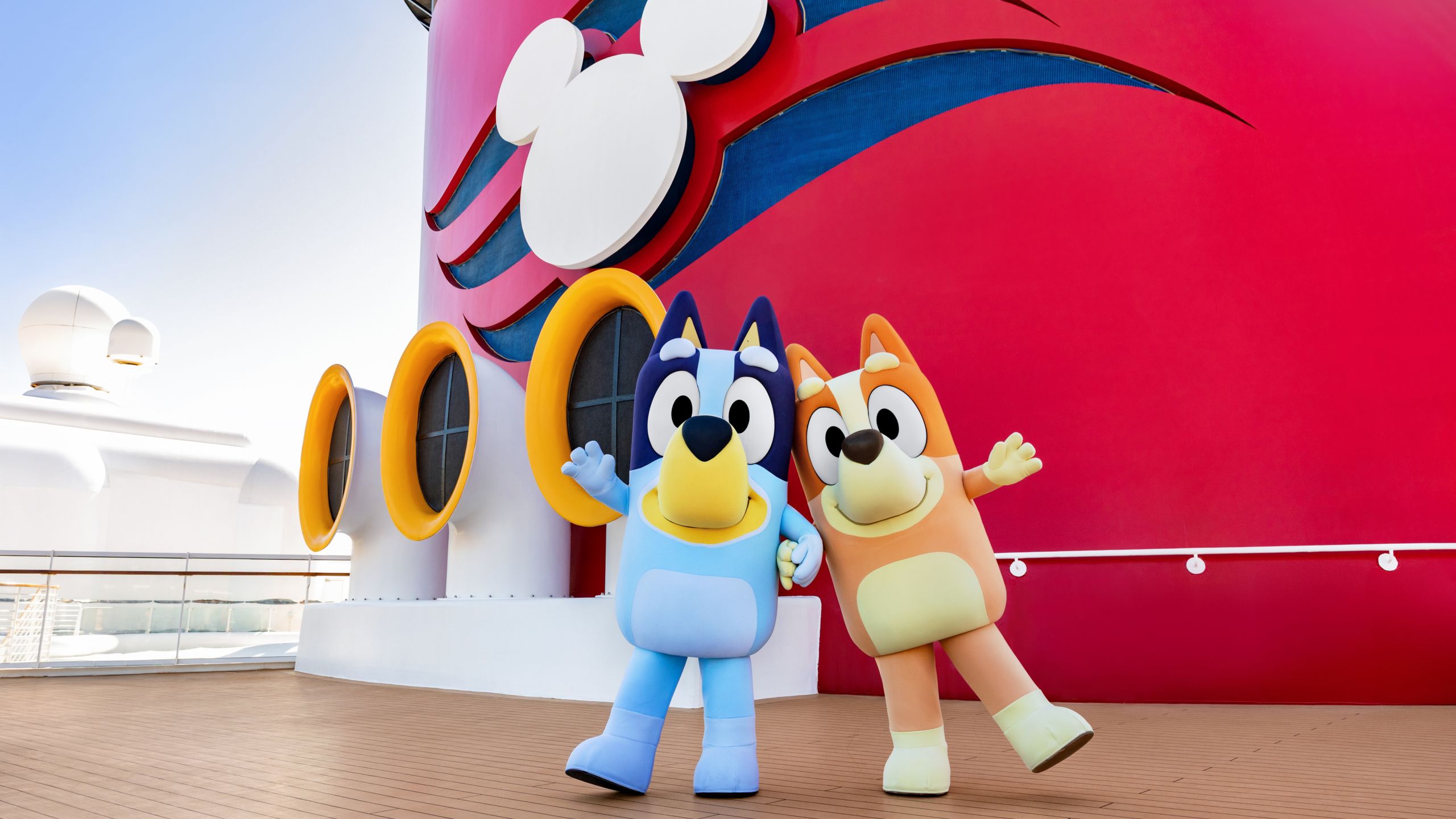 Bluey and Bingo standing next to a ship’s funnel on the top deck of a Disney cruise ship